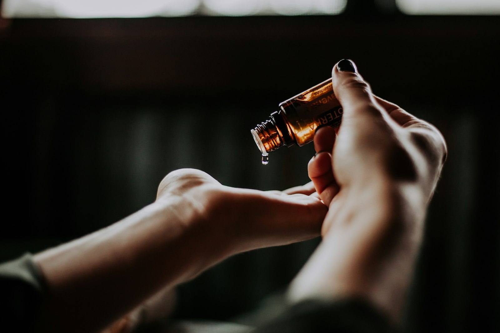 A drop of aromatherapy oil falling from a small amber bottle into an open palm